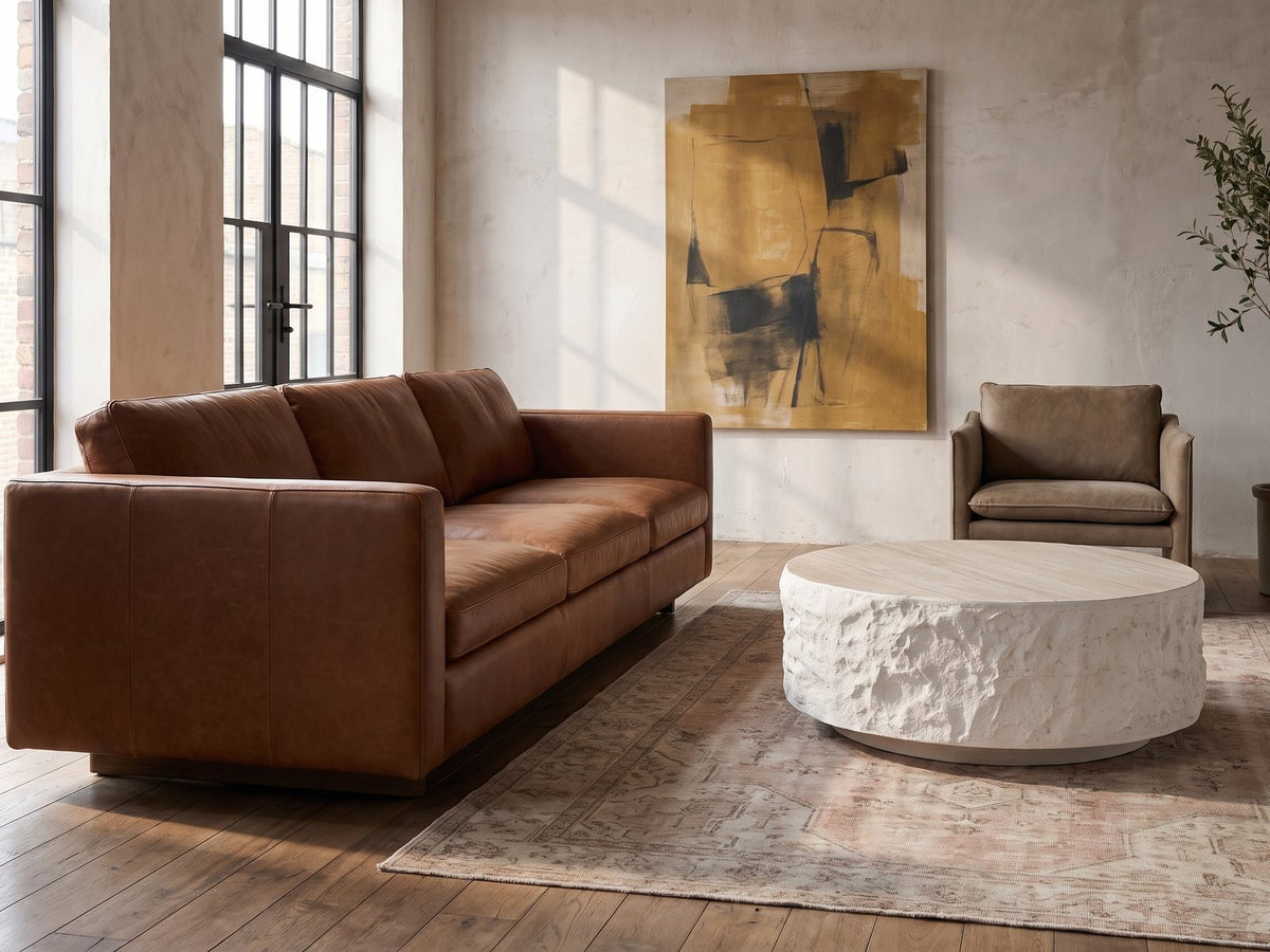 Piombino Faux Travertine Fiberglass Drum Coffee Table on a vintage rug in front of a leather sofa in an industrial loft