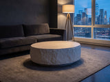 Piombino Faux Travertine Fiberglass Drum Coffee Table on a wool rug in front of a velvet sofa in a city penthouse at blue hour