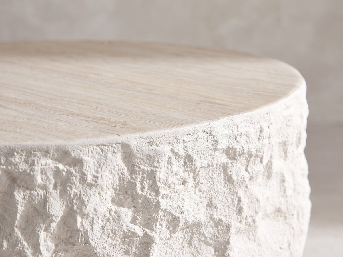 Close-up of the Piombino Faux Travertine Fiberglass Drum Coffee Table: the rock-face side rising to the travertine-look top