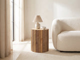 Pisticci Solid Mango Fluted Drum Side Table with a lamp and a ceramic bowl beside a cream boucle armchair in a bright plaster room