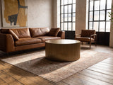 Pitigliano Brass-Finish Fluted Drum Coffee Table on a vintage rug in front of a leather sofa in an industrial loft