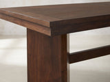 Close-up of the Pizzo 76-Inch Walnut Veneer Extending Trestle Dining Set with Bench and 4 Chairs: a thick walnut slab leg under the stepped edge of the top