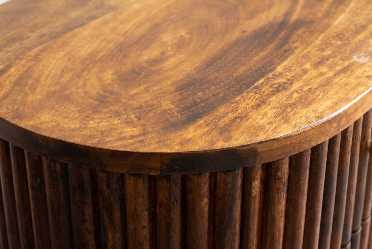 Close-up of the oval mango wood top of the Ploaghe nightstand, with swirling golden-brown grain above the fine vertical reeds