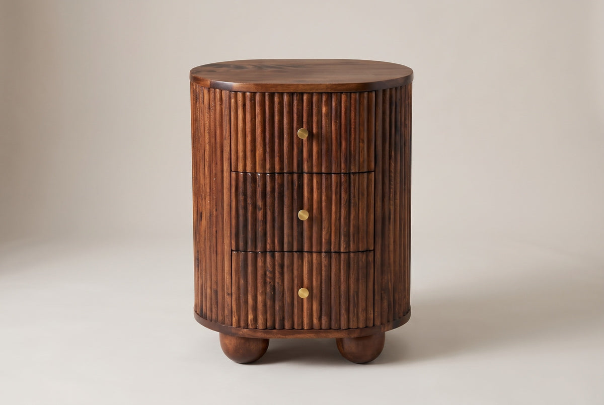The Ploaghe nightstand in chestnut mango wood, front view on a light studio backdrop: three reeded drawers with brass knobs and two round feet