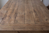 Close-up of the fir plank top of the Policoro dining table: weathered brown boards with fine seams, knots and saw marks, and the breadboard end