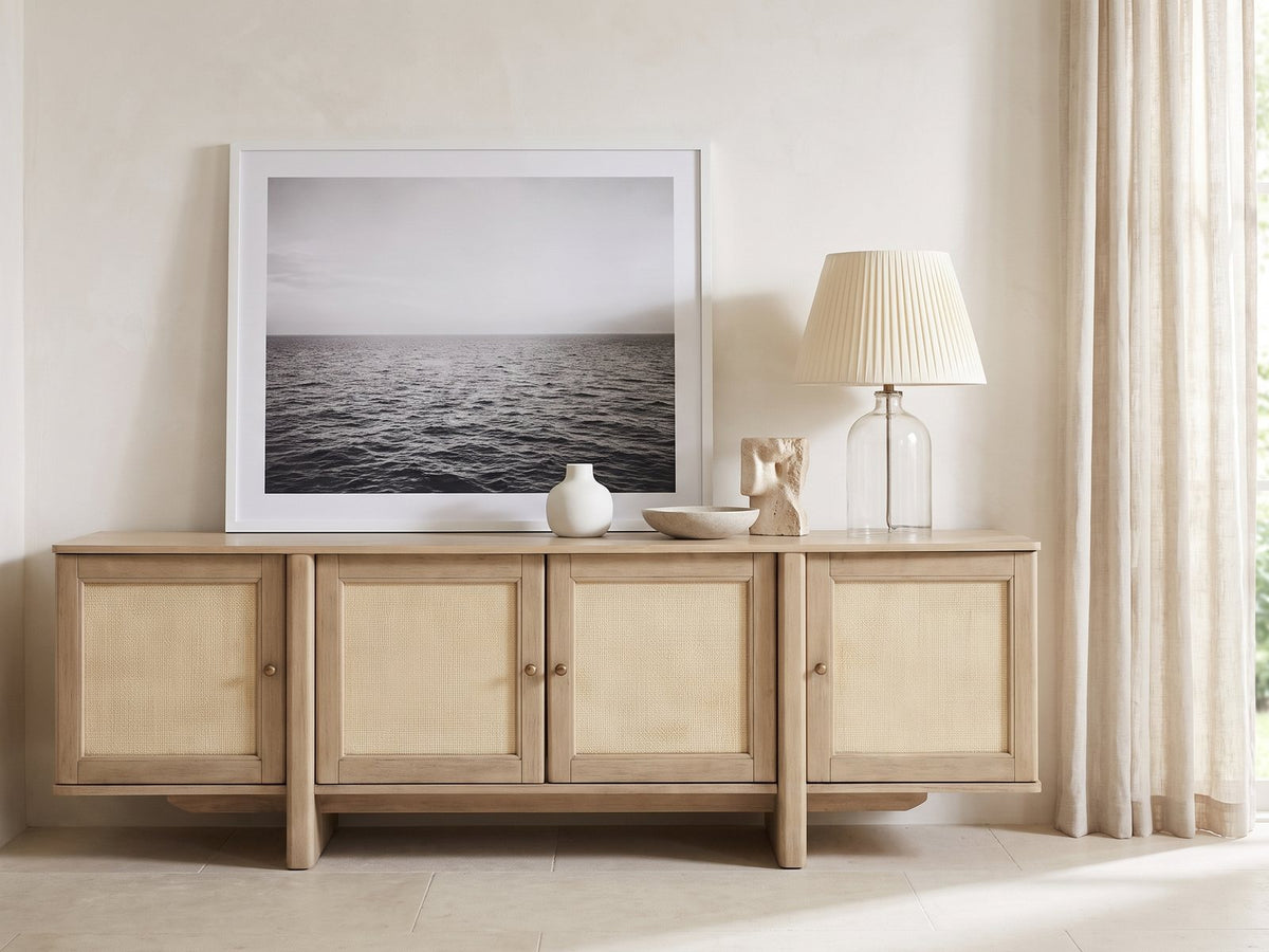 Polignano Oak and Cane Media Console styled with a leaning print, a lamp and ceramics in a bright plaster room