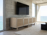 Polignano Oak and Cane Media Console seen from the side, under a wall-mounted screen on a pale stone wall in a poolside villa