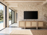 Polignano Oak and Cane Media Console under a wall-mounted screen on a pale stone wall in a poolside villa