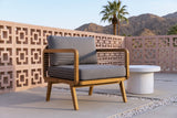 Polizzi acacia lounge armchair on concrete pavers on a Palm Springs patio at golden hour, a terracotta-pink breeze-block wall, a fan palm and the desert mountains behind (side table not included)