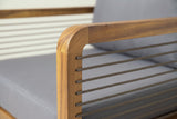 Close-up of a Polizzi arm: the rounded corner of the teak-finish acacia frame and taupe braided rope strands threaded through it, the grey cushion behind