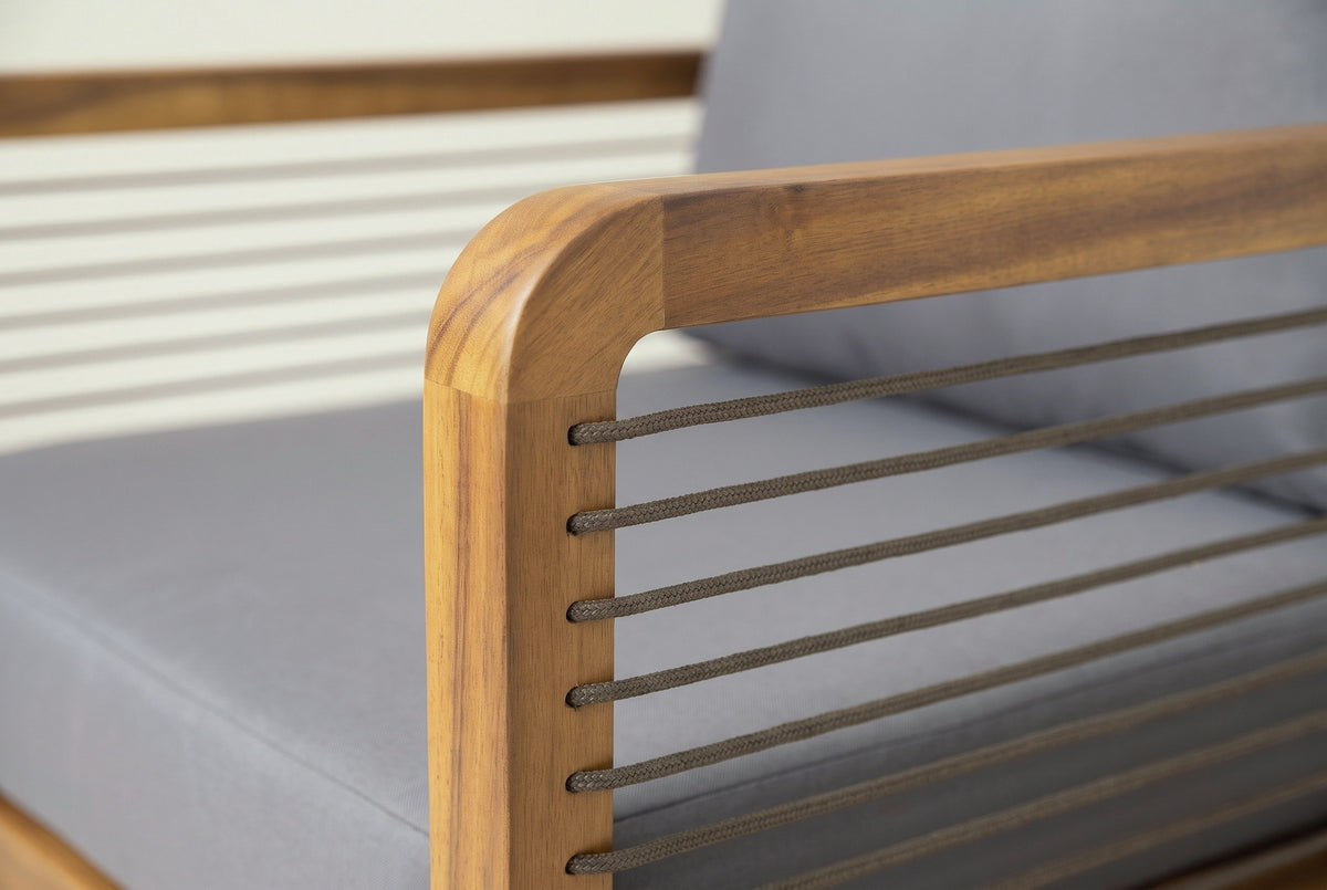Close-up of a Polizzi arm: the rounded corner of the teak-finish acacia frame and taupe braided rope strands threaded through it, the grey cushion behind
