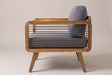 The Polizzi lounge armchair seen from the side: one rounded acacia frame with ten horizontal rope strands, the grey cushions behind and the legs angling out front and back