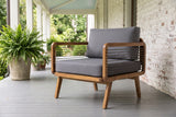 Polizzi acacia lounge armchair on a covered porch in Wilmington, North Carolina, with a whitewashed brick wall, grey porch boards and potted ferns (planters not included)
