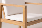 Close-up of a Pollina chair: the acacia arm rail and front post in a light teak finish, a small bolt cap and the ivory seat cushion