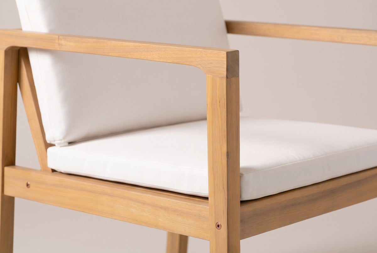 Close-up of a Pollina chair: the acacia arm rail and front post in a light teak finish, a small bolt cap and the ivory seat cushion
