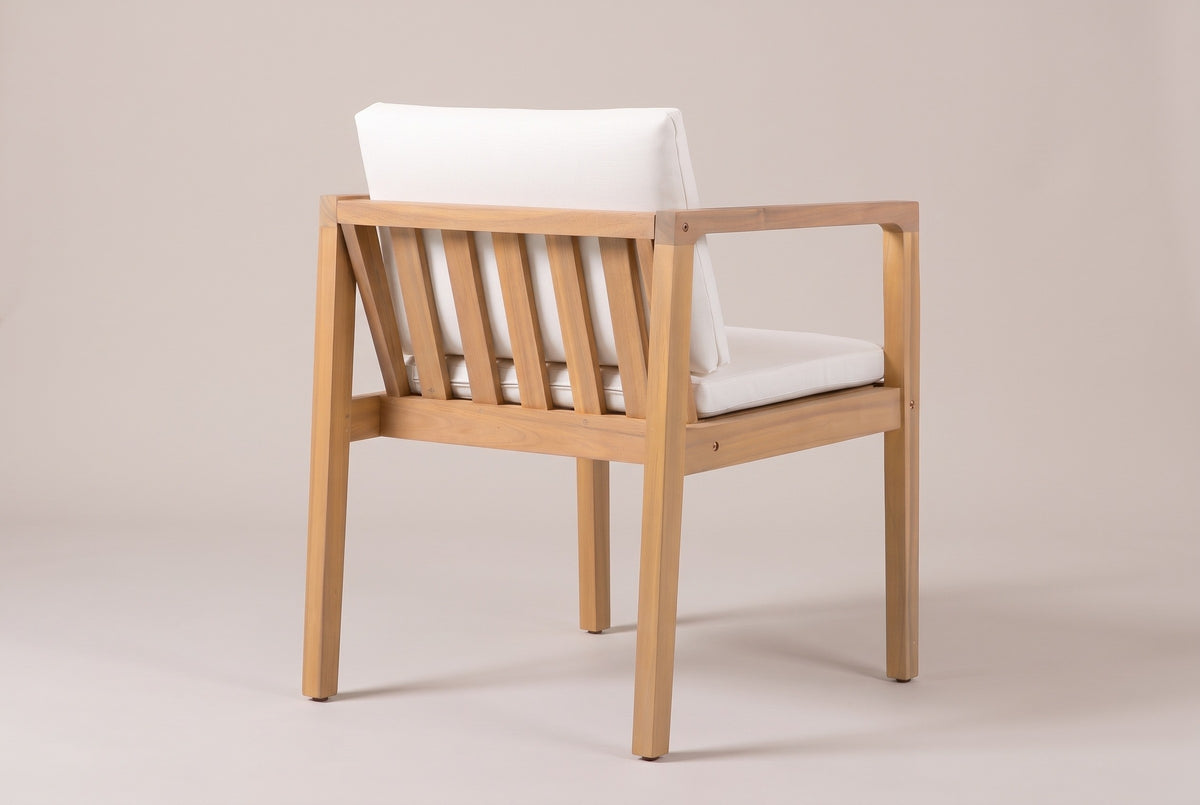 A Pollina dining armchair seen from behind: the reclined back with five vertical acacia slats, the ivory back cushion above it