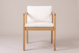 A Pollina dining armchair from the front: flat arms on square posts, a deep seat rail, the ivory seat and back cushions
