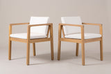 The two Pollina acacia dining armchairs with ivory cushions, three-quarter view on a light studio backdrop