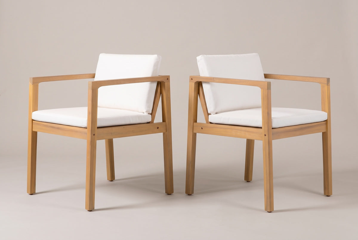 The two Pollina acacia dining armchairs with ivory cushions, three-quarter view on a light studio backdrop