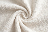 Close-up of the cream boucle on the Pollutri bed: small, curly off-white loops gathered in a soft swirl