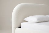 One top corner of the Pollutri headboard: a big, smooth rounded curve in cream boucle above a white mattress and pillow