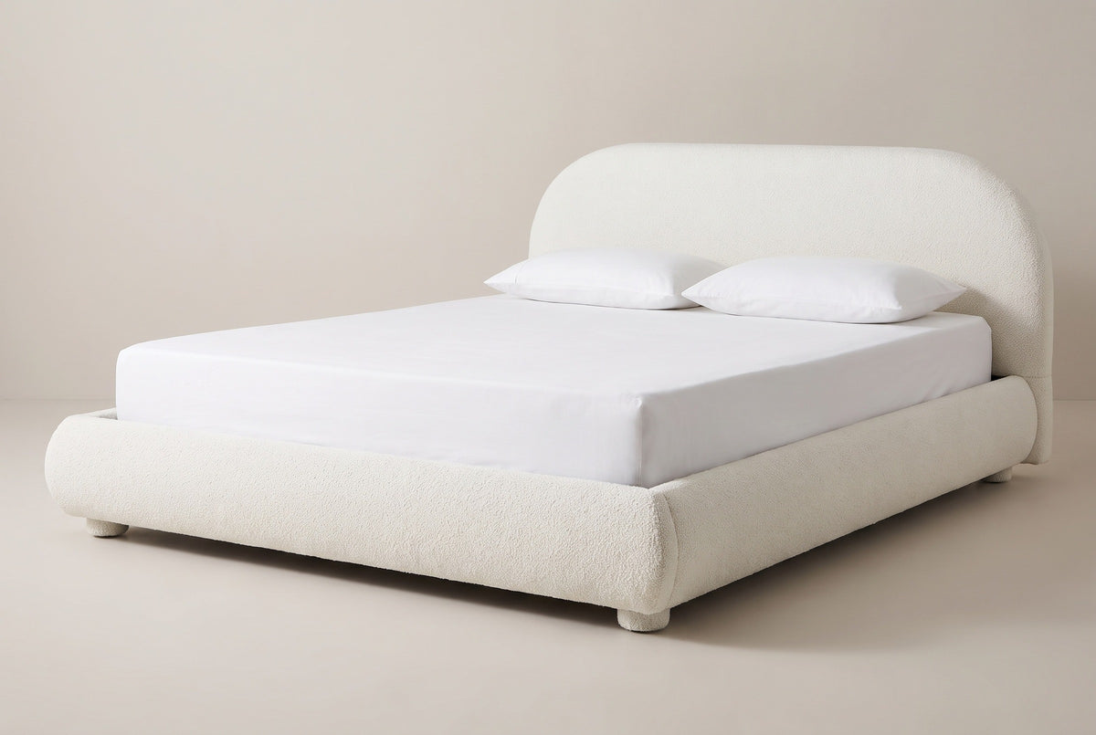 The Pollutri bed in cream boucle with a white mattress and pillows (not included), three-quarter view on a light studio backdrop