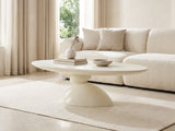 Ponza Milk White Fiberglass Pebble Coffee Table styled with books, a vase and a stone bowl in front of a cream sofa in a bright plaster room