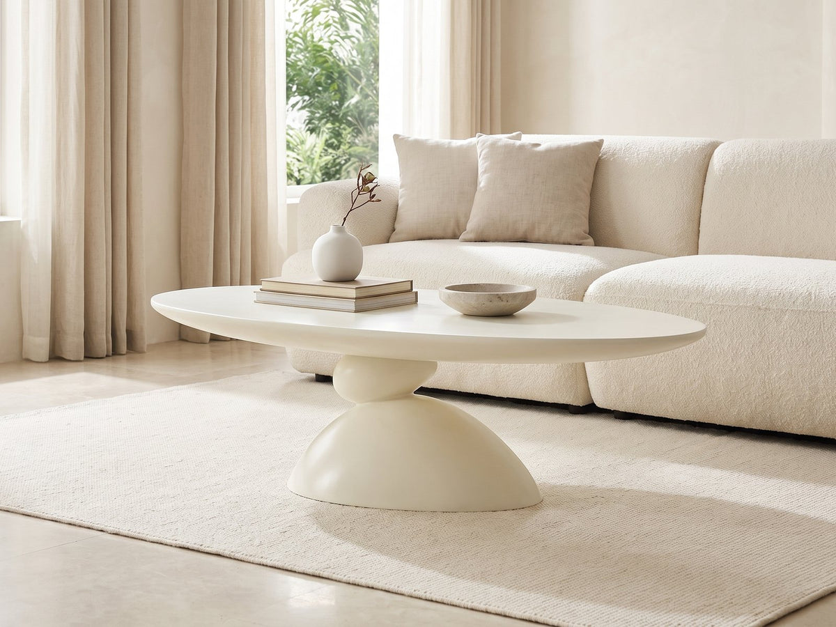 Ponza Milk White Fiberglass Pebble Coffee Table styled with books, a vase and a stone bowl in front of a cream sofa in a bright plaster room