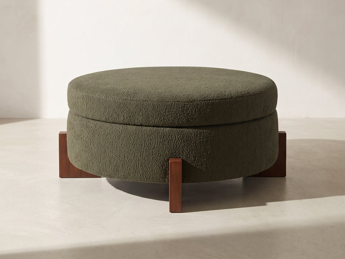 Portofino Round Storage Ottoman in olive green against a plaster wall in morning light