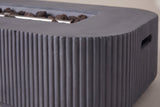 Close-up of the Portopalo fire pit: dark gray fluted concrete turning round a corner under the smooth top rim, lava rocks in the burner