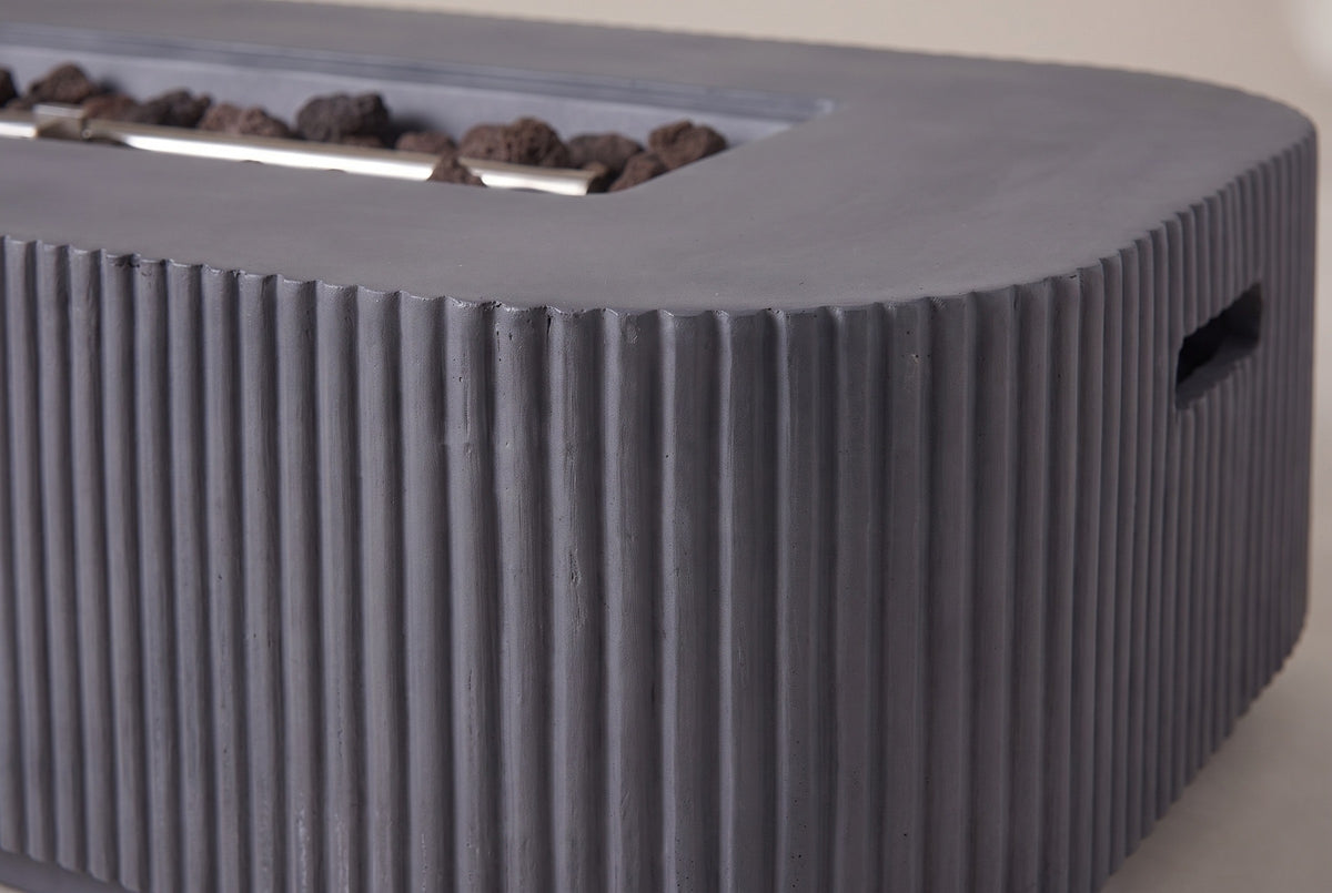 Close-up of the Portopalo fire pit: dark gray fluted concrete turning round a corner under the smooth top rim, lava rocks in the burner