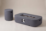 The Portopalo fire pit and its round fluted companion piece in dark gray concrete, three-quarter view on a light studio backdrop