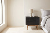 Posada black oak two-drawer nightstand with a ceramic lamp beside a bed in a Scottsdale bedroom with an ivory plaster wall and an arched window