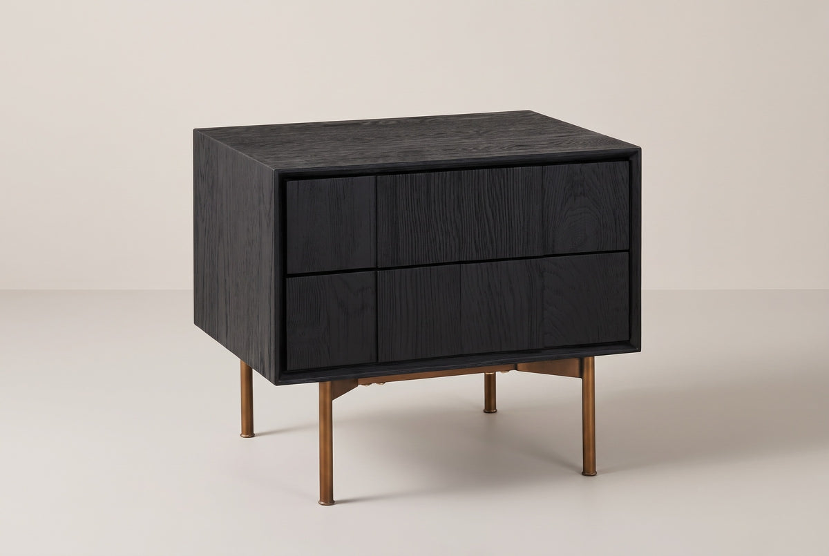 The Posada two-drawer nightstand in black wire-brushed oak on four bronze-finish legs, three-quarter view on a light studio backdrop