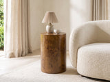 Potenza Walnut Burl Pillar Side Table with a lamp and a ceramic bowl beside a cream boucle armchair in a bright plaster room