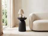 Presicce Black Mango Scalloped Pedestal Side Table with a lamp and a ceramic bowl beside a curved cream boucle seat in a bright plaster room