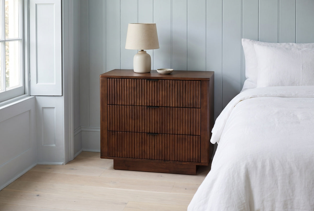 Pula reeded walnut nightstand with a ceramic lamp in a Charleston townhouse bedroom with pale blue-grey wood panelling and white oak floors
