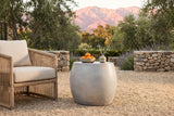 Racalmuto concrete barrel side table with a bowl of oranges and a small vase of olive on a gravel terrace in Ojai, California at golden hour, a river-stone wall, olive trees and the mountains behind (chair and decor not included)