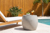 Racalmuto light grey concrete barrel side table with a bowl of limes and a glass of iced tea beside a teak lounger on a limestone pool terrace in Sarasota, a cedar slat wall behind (lounger and decor not included)
