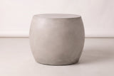 The Racalmuto side table seen straight from its long side: a wide light grey barrel, widest a little above the middle