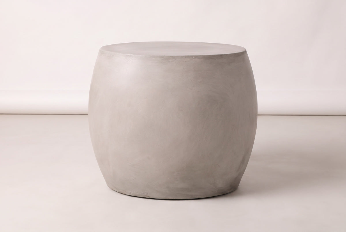 The Racalmuto side table seen straight from its long side: a wide light grey barrel, widest a little above the middle