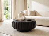 Radda Black Carved Wood Drum Coffee Table styled with books, a vase and a stone bowl in front of a cream sofa in a bright plaster room