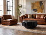 Radda Black Carved Wood Drum Coffee Table on a vintage rug in front of a leather sofa in an industrial loft