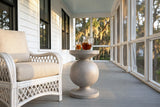 Raffadali concrete sphere pedestal side table with a pitcher of iced tea and a glass beside a white wicker armchair on a screened porch in Beaufort, South Carolina, white clapboard, grey floorboards and live oaks with Spanish moss outside (chair and decor not included)