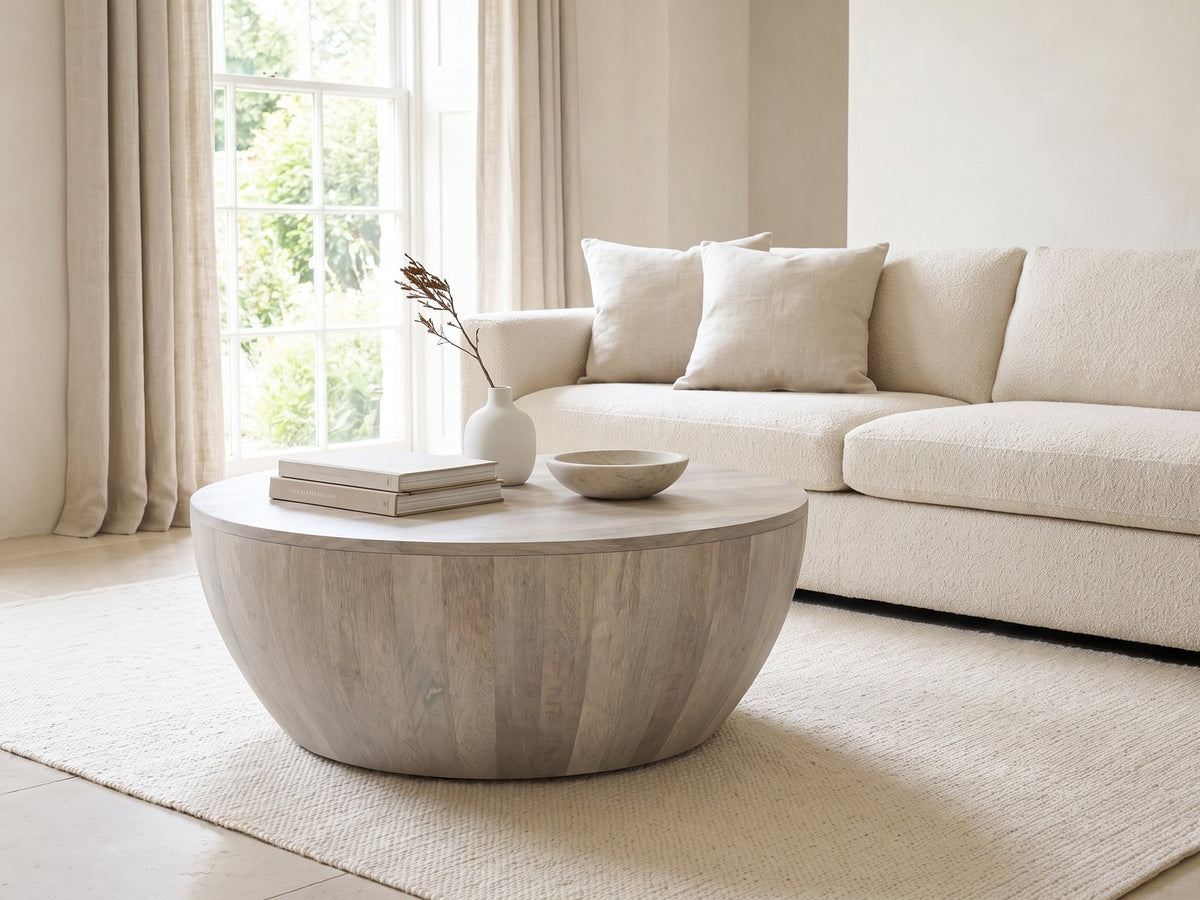 Rapallo Whitewashed Mango Bowl Coffee Table styled with books, a vase and a stone bowl in front of a cream sofa in a bright plaster room