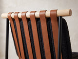 Close-up of the Rende 59-Inch Round Black Oak Hourglass Dining Set with 6 Chairs: cognac straps over a pale oak rail on the back of a black boucle chair