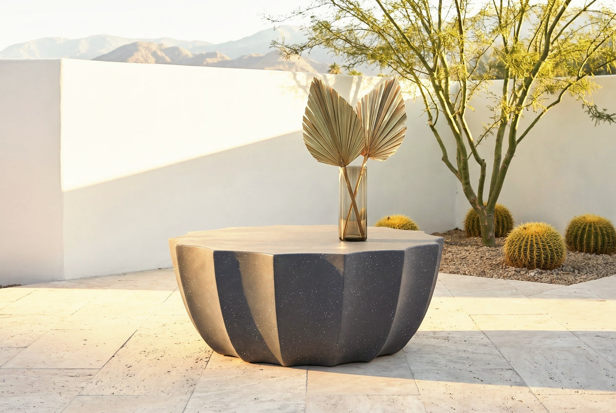 Ribera speckled gray coffee table on pale travertine in a Palm Desert courtyard at golden hour, a white stucco wall, a palo verde tree, barrel cacti and mountains behind (vase not included)