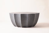 The Ribera coffee table seen from the side: the thin edge of the top over the fluted bowl body tapering toward the base