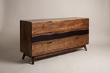 The Rionero six-drawer sideboard in amber-brown acacia with a dark band across the middle row, three-quarter view on a light studio backdrop
