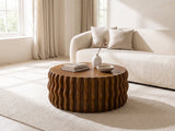 Rivoli 30-Inch Round Carved Wood Drum Coffee Table styled with books, a vase and a stone bowl in front of a cream sofa in a bright plaster room
